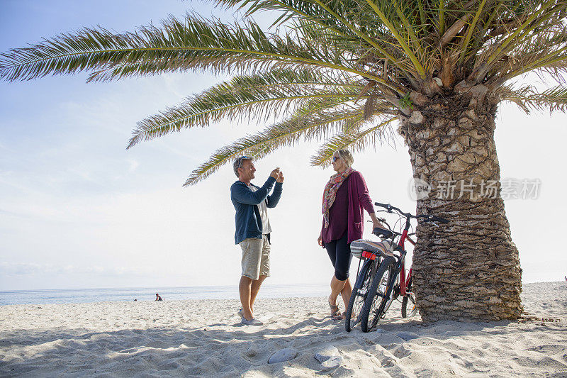 一对夫妇骑着自行车在早上沿着热带海滩散步