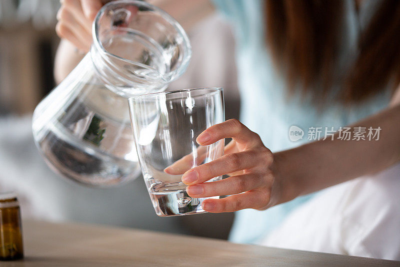 妇女把水从罐子倒进玻璃杯里，服用补品