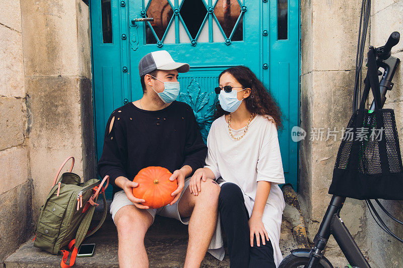 一对年轻的学生戴着保护面具，骑着电动滑板车在老城探险后带着南瓜休息