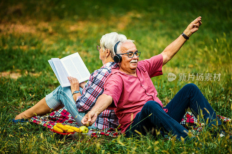 一对很棒的老夫妇正在公园里休息，一边看书，一边听音乐