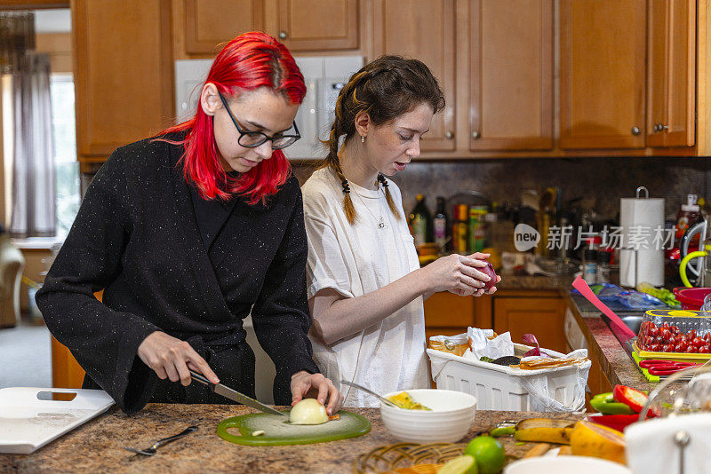 两个十几岁的女孩在自家厨房做饭，准备晚餐。一个在切蔬菜，另一个在剥蔬菜的背景。