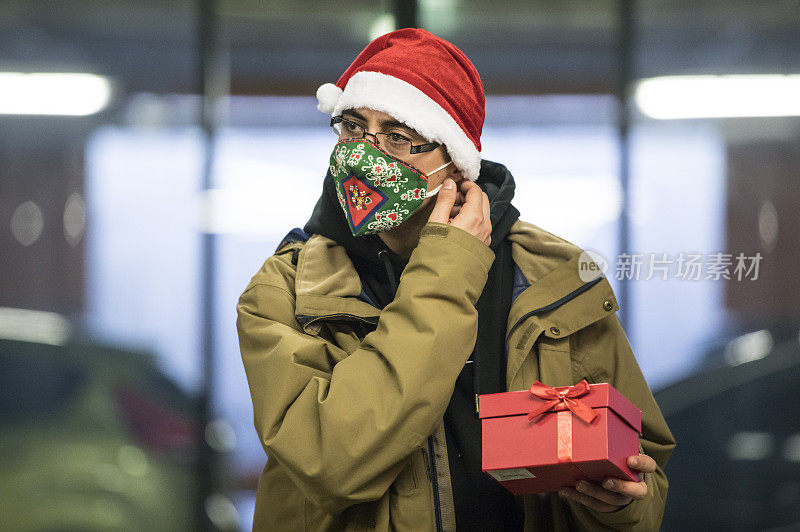新冠肺炎疫情期间，一名年轻男子拿着圣诞礼物离开购物中心时摘下防护口罩