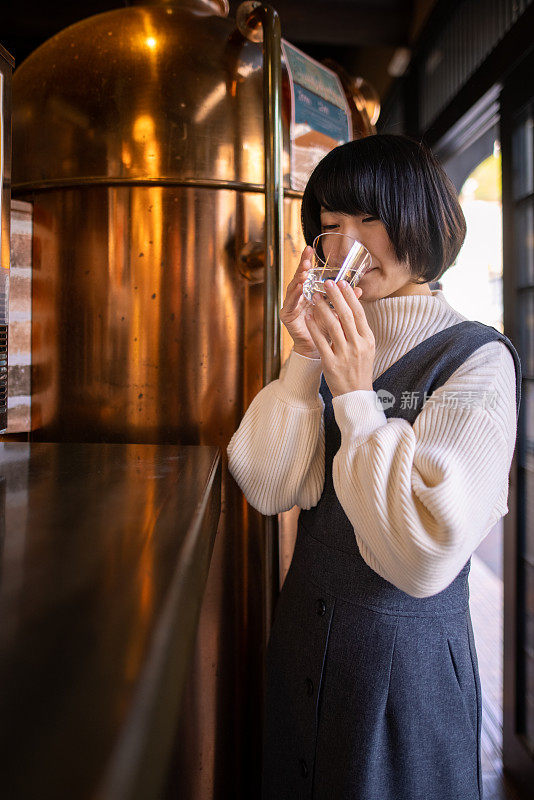 年轻女子喝一杯“saki”(日本米酒)在酒类商店