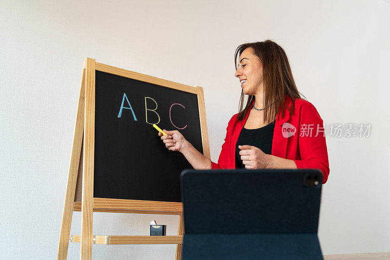 女教师正试图用她在黑板上的数字平板电脑教她远处的学生字母表