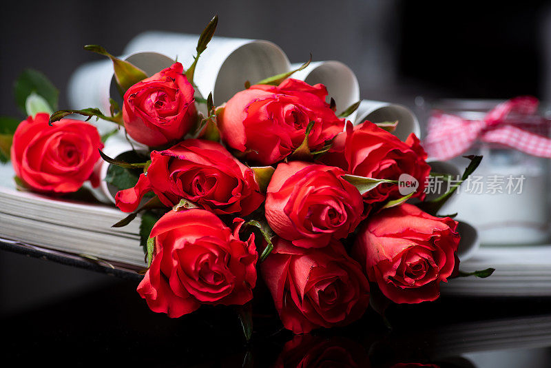 红玫瑰花和一本书摆放在深色的桌子上