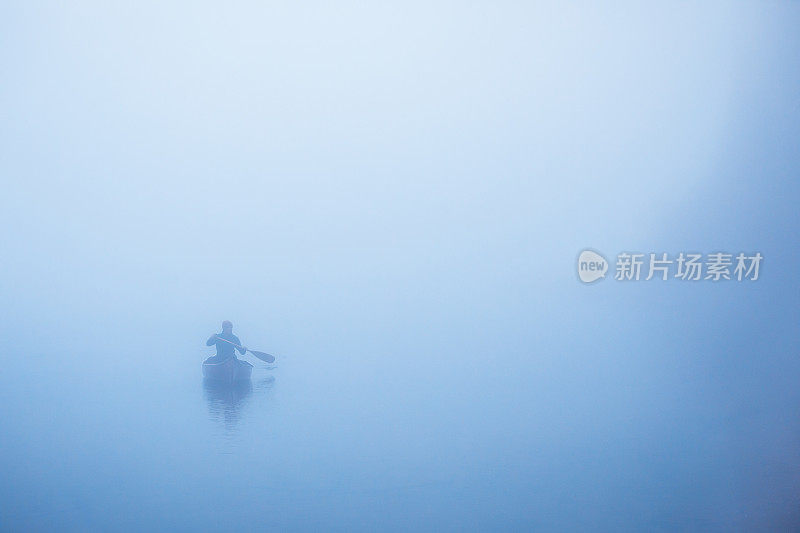 在阴沉阴沉的天气里，人们在平静的湖面上划独木舟。