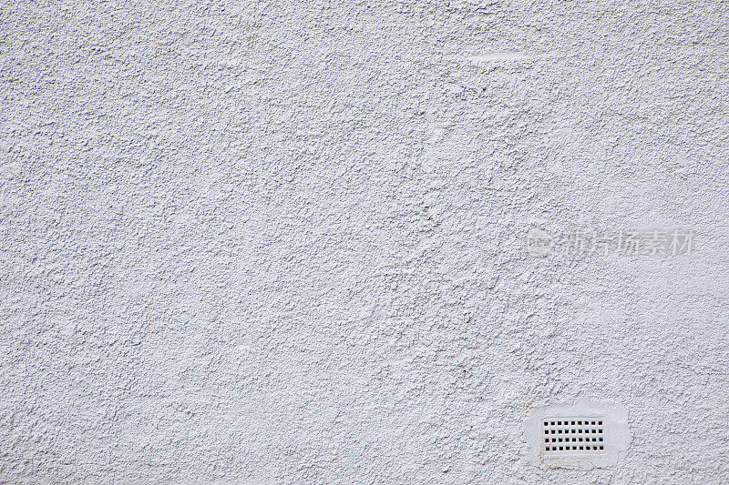 白色粗糙的灰泥墙，底部角落有一块空气砖