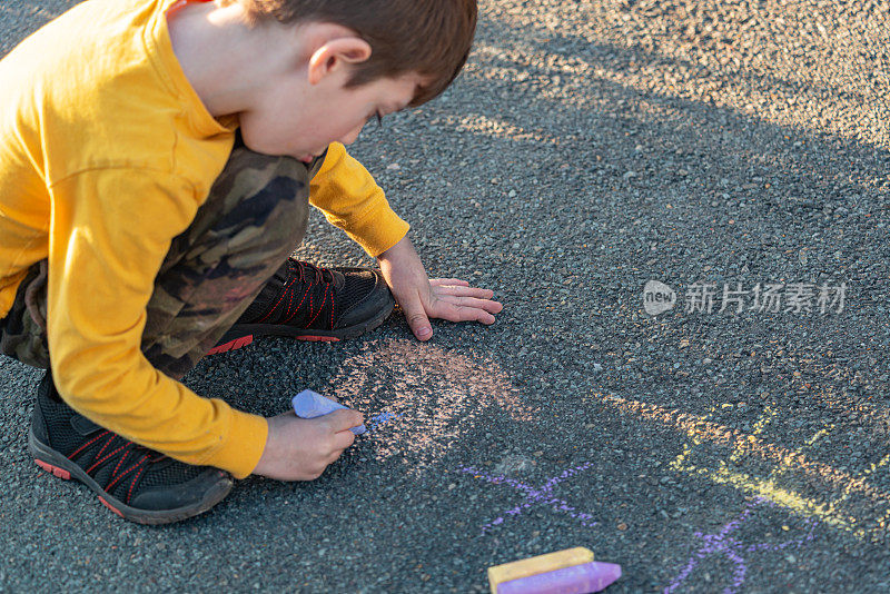 男孩在车道上用粉笔画画