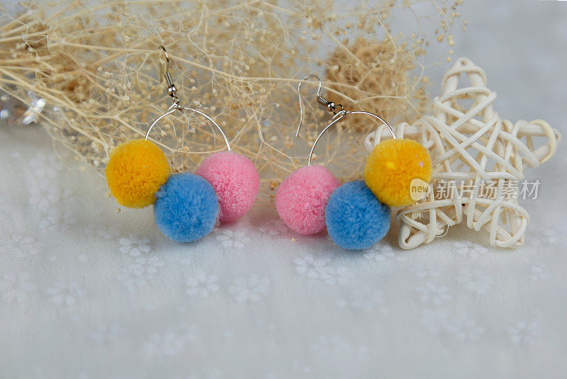 三个毛绒球形状的彩色绒球耳环。耳环旁边是藤制品、花卉标本和其他装饰品