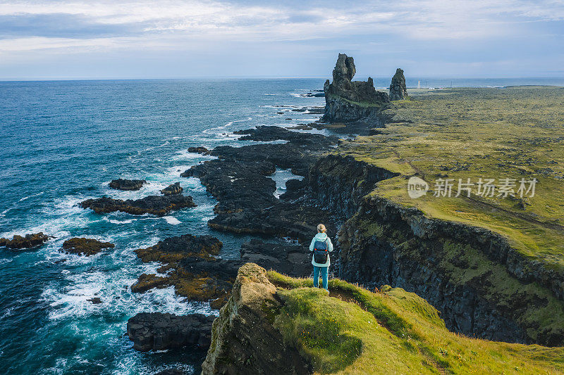 一名穿着黄色夹克的男子站在冰岛户外公园的岩石顶端。Londrangar