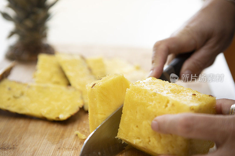 一个女人的手用刀在一块板上切菠萝片的特写