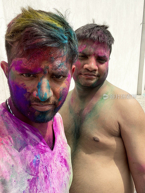 图片中的两名印度教徒，一个穿着Kurta传统服装，另一个赤裸上身，覆盖着油漆粉末颜色，在胡里节的色彩和爱漆斗争中嬉戏，微笑着看着相机