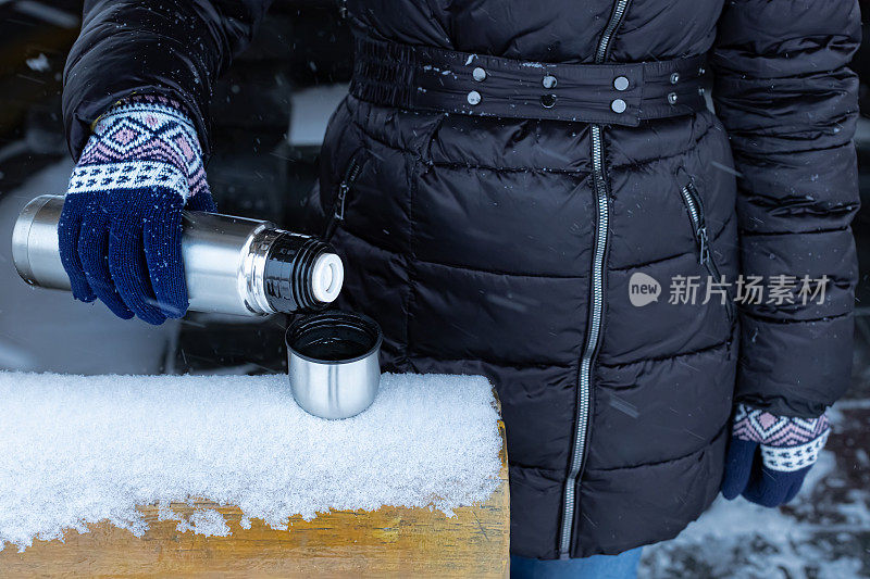 冬天的街道上，一名妇女从保温瓶里把茶倒进保温瓶里