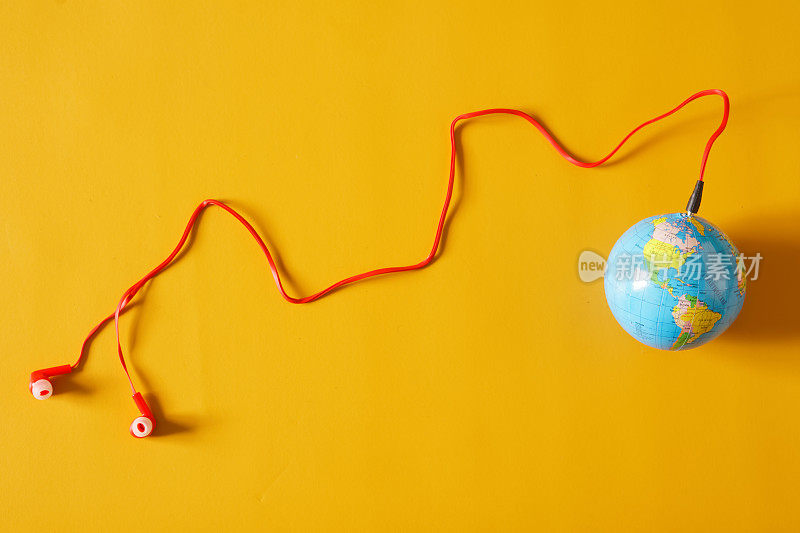 红色的有线耳塞与一个小地球仪相连。广播的概念、网络广播、播客和广播世界各地流行的热门音频
