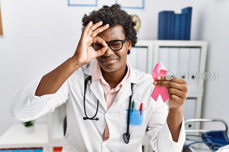 非洲医生男人拿着粉色的癌症丝带，微笑着，开心，做得好，手放在手上，看着手指