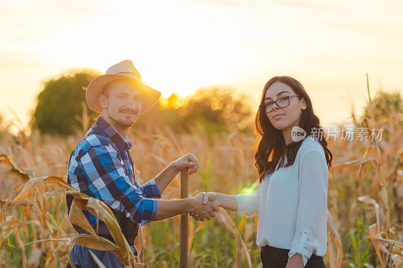 一个穿着蓝色衬衫的年轻男性农民与一位女性农业检查员握手的齐腰照片