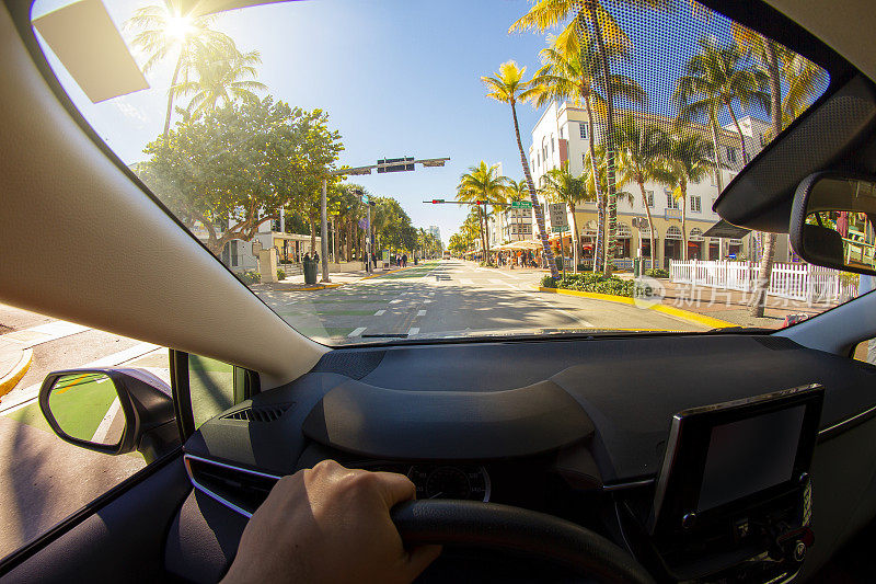 一个年轻的运动男子的视角拍摄在迈阿密海滩艺术装饰区，迈阿密，南佛罗里达，美国，在天堂蓝色的海洋景观前驾驶一辆汽车