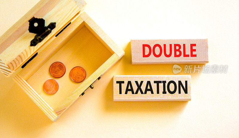 双重征税的象征。概念词对漂亮的白色桌子上的木块征收双重税白色背景。装着硬币的木箱。营业税和双重征税的概念，复制空间。