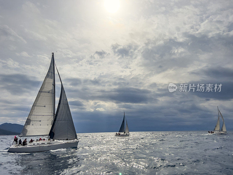 三艘帆船与船员在多云的日子航行在赛船会，天空大海的背景