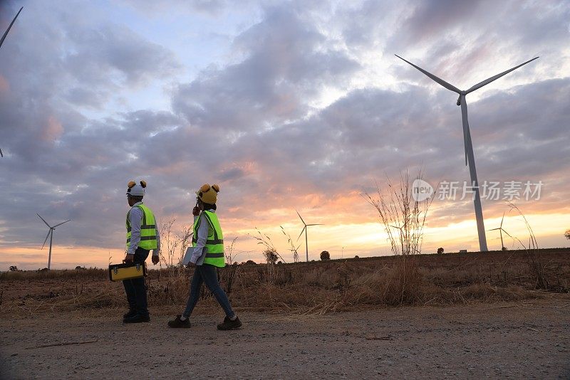 男、女工程师同事扛着工具和设备箱走在风力发电机组，可再生和绿色能源的概念