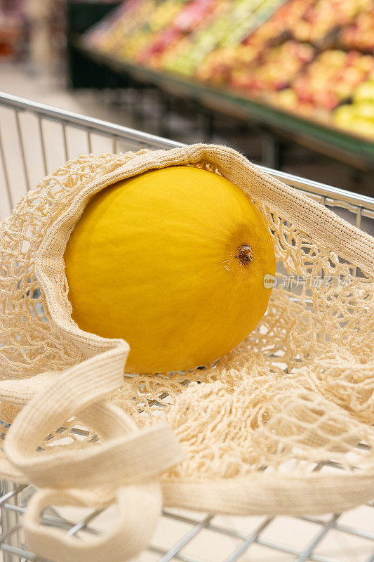 黄色的瓜装在可重复使用的网状购物袋里，背景是超市。