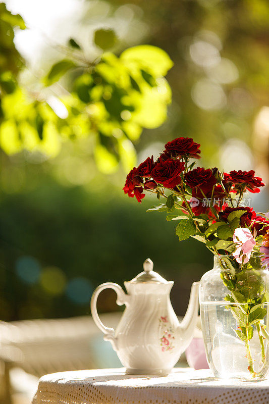 美丽的红玫瑰作为下午茶的装饰在阳光明媚的花园里
