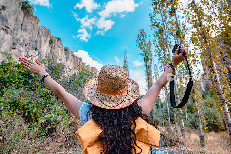 土耳其Aksaray的Peristrema山谷的Ihlara山谷，一个旅行摄影师女孩拿着相机在秋天张开双臂