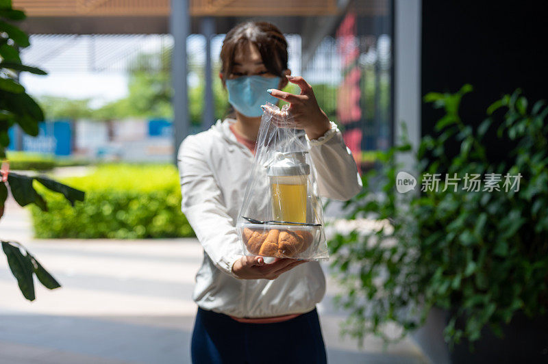 妇女戴着口罩，使食品杂货给烘焙食品盒塑料袋和果汁在前面的房子股票照片…