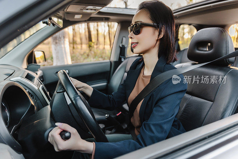亚洲女人开着车，面带微笑。一个年轻成功快乐的女人正在开车。