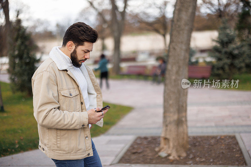 年轻男子在城市公园散步时使用手机