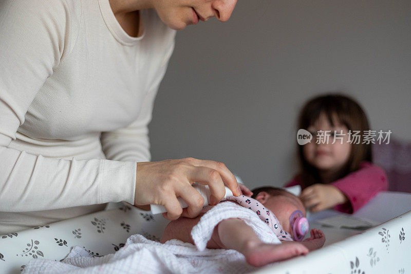 母亲清洗新生儿的肚脐。姐姐看着她的妈妈和孩子。