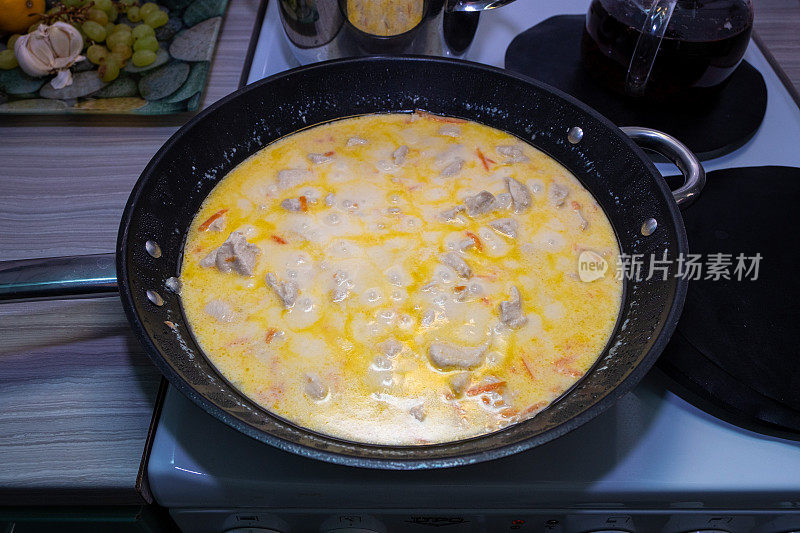 鸡肉块在一个大煎锅里用奶油酱煮熟，食物在炉子上煮。