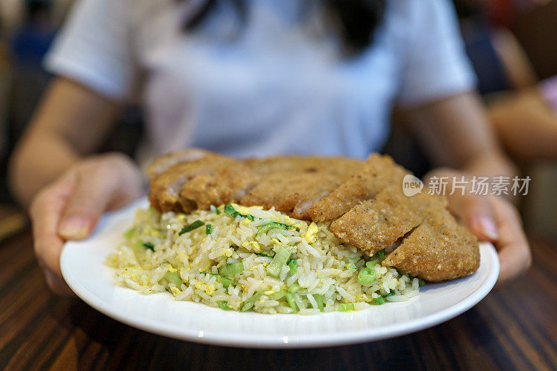 一个亚洲女人在餐馆里拿着一盘猪排炒饭，准备吃。