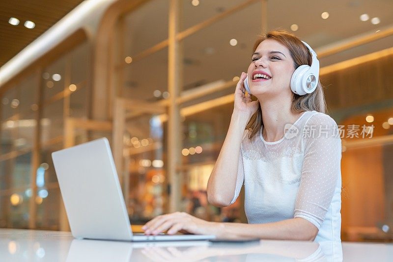 随意的商务女性，使用笔记本电脑和耳机，在带咖啡厅的工作空间进行电子学习和视频会议