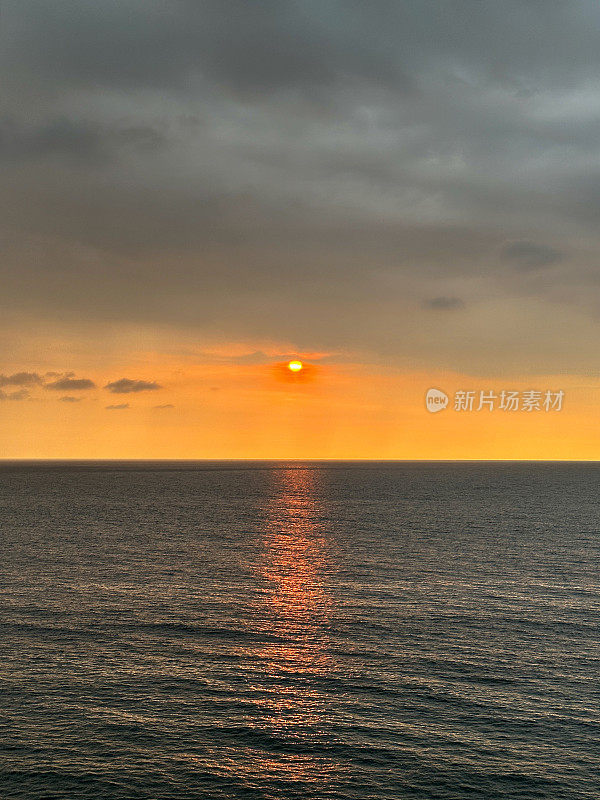 太阳在海洋地平线上戏剧性的橙色天空中落下的图像，忧郁的灰色云岸，太阳在水中的反射