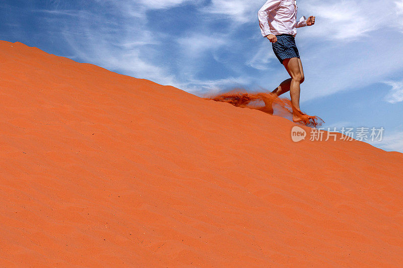 一个游客正从沙丘上跑下来，踢起尘土