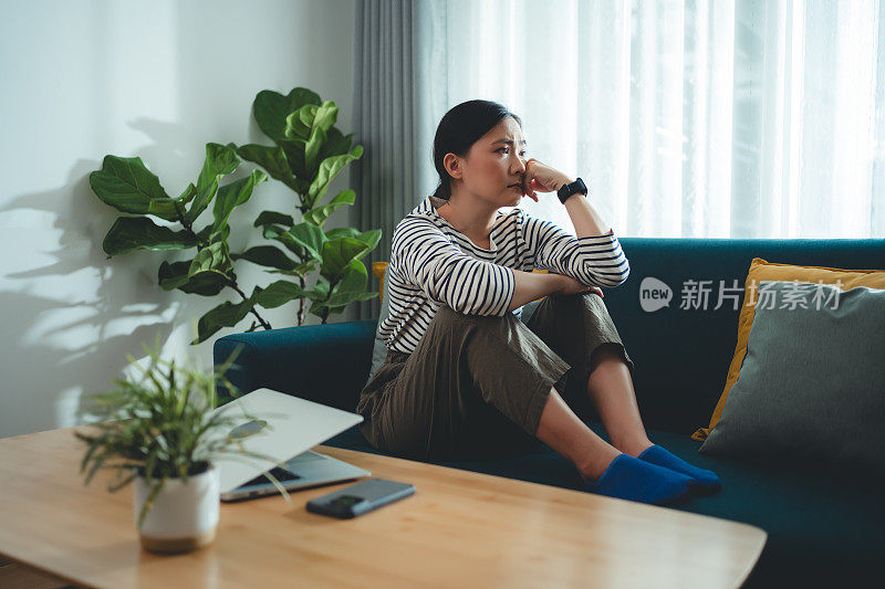 亚洲女人抱膝坐在沙发上思考问题，感到孤独。