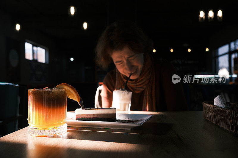 一个开朗的成熟女人坐在昏暗的咖啡馆里喝咖啡
