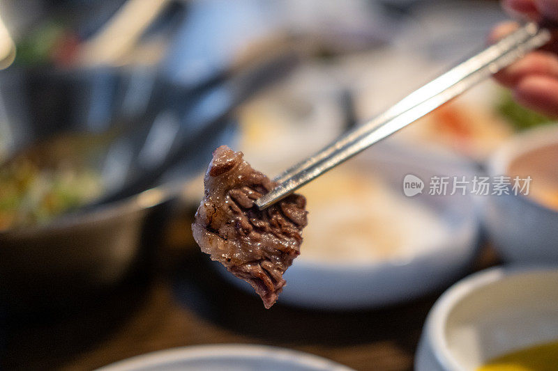 筷子夹着一块韩式烤肉。烧烤肉与软焦点
