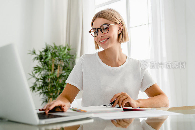 年轻的白人女性自由职业者使用笔记本电脑在家里的办公桌上进行电子学习。