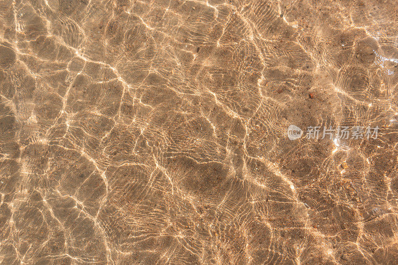 美丽的清澈的水与光的反射和波浪在黄色沙滩上，俯视图。抽象水的纹理。暑假在红海