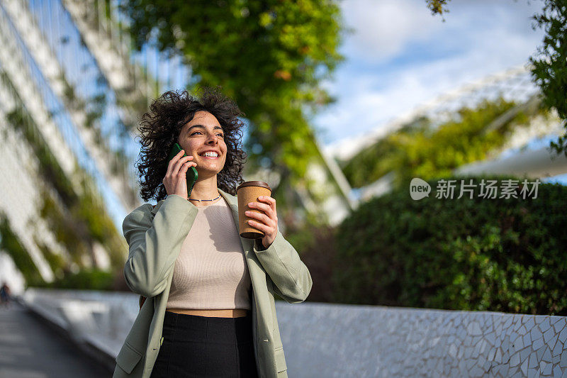 欢快的女人一边拿着咖啡一边讲着手机。