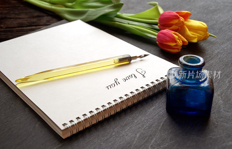 旧钢笔和词“我爱你”在纸笔记本上的黑色背景与鲜花和墨水瓶
