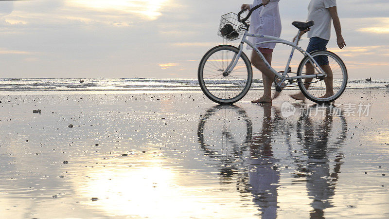 成熟的夫妇在日出时把自行车推下海滩