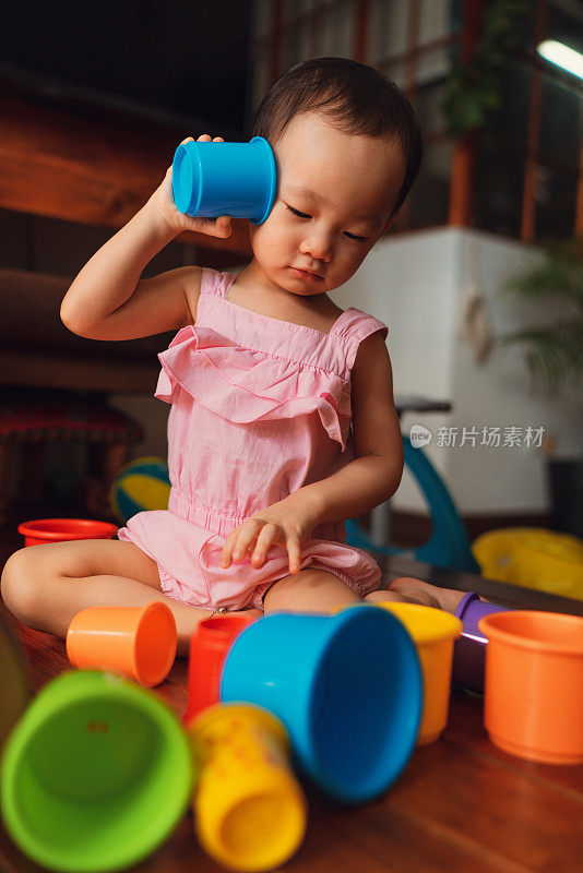 一个富有表现力的亚洲蹒跚学步的孩子在家里玩五颜六色的堆叠杯子