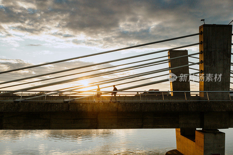 日落时分，两个人在桥上骑着电动滑板车