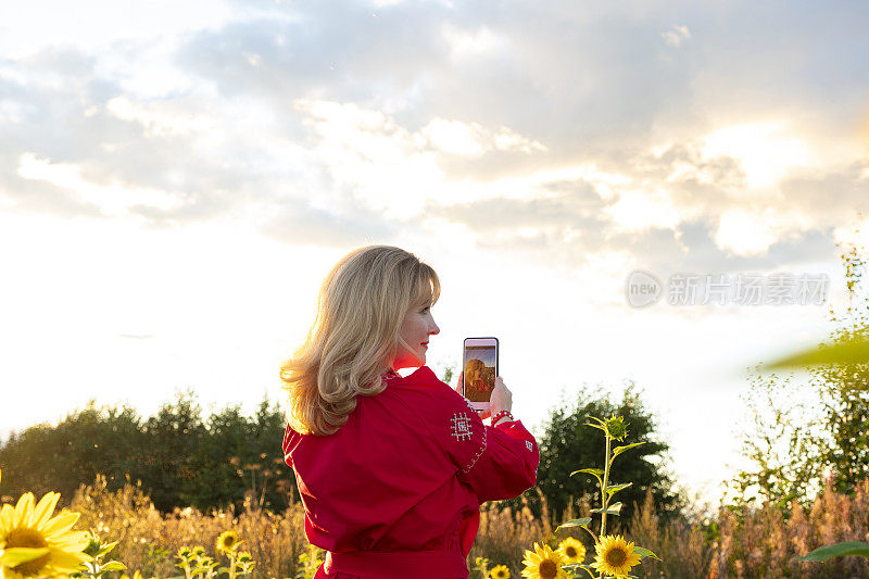 穿着红色衣服的年轻白人女人。在日落的背景下自拍。乡间的向日葵田。