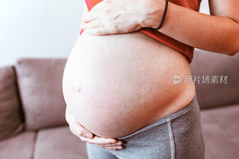 一个年轻的孕妇抱着她的肚子的特写