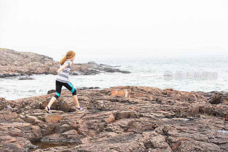 女孩在苏必利尔湖岸边的岩石上奔跑