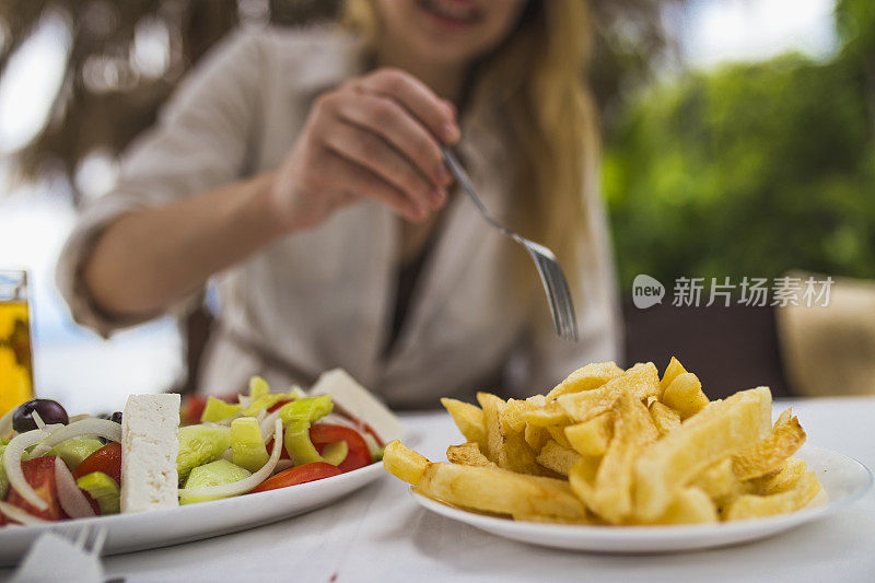 一个女人在海边的餐馆里吃着希腊沙拉和薯条